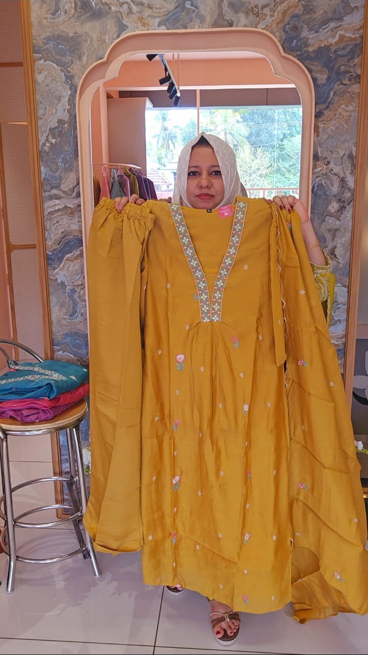 Woman holding a yellow dress with intricate designs in front of a mirror.
